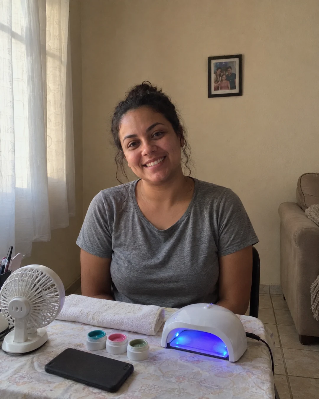 Aline sorrindo na mesa de manicure montada na sala de casa